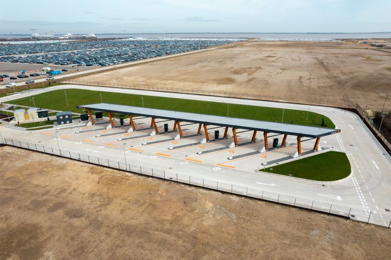 Aerial drone photo of the finished Immingham Charging Hub: a long canopy over charging bays, set in open graded ground beside a large car storage yard.