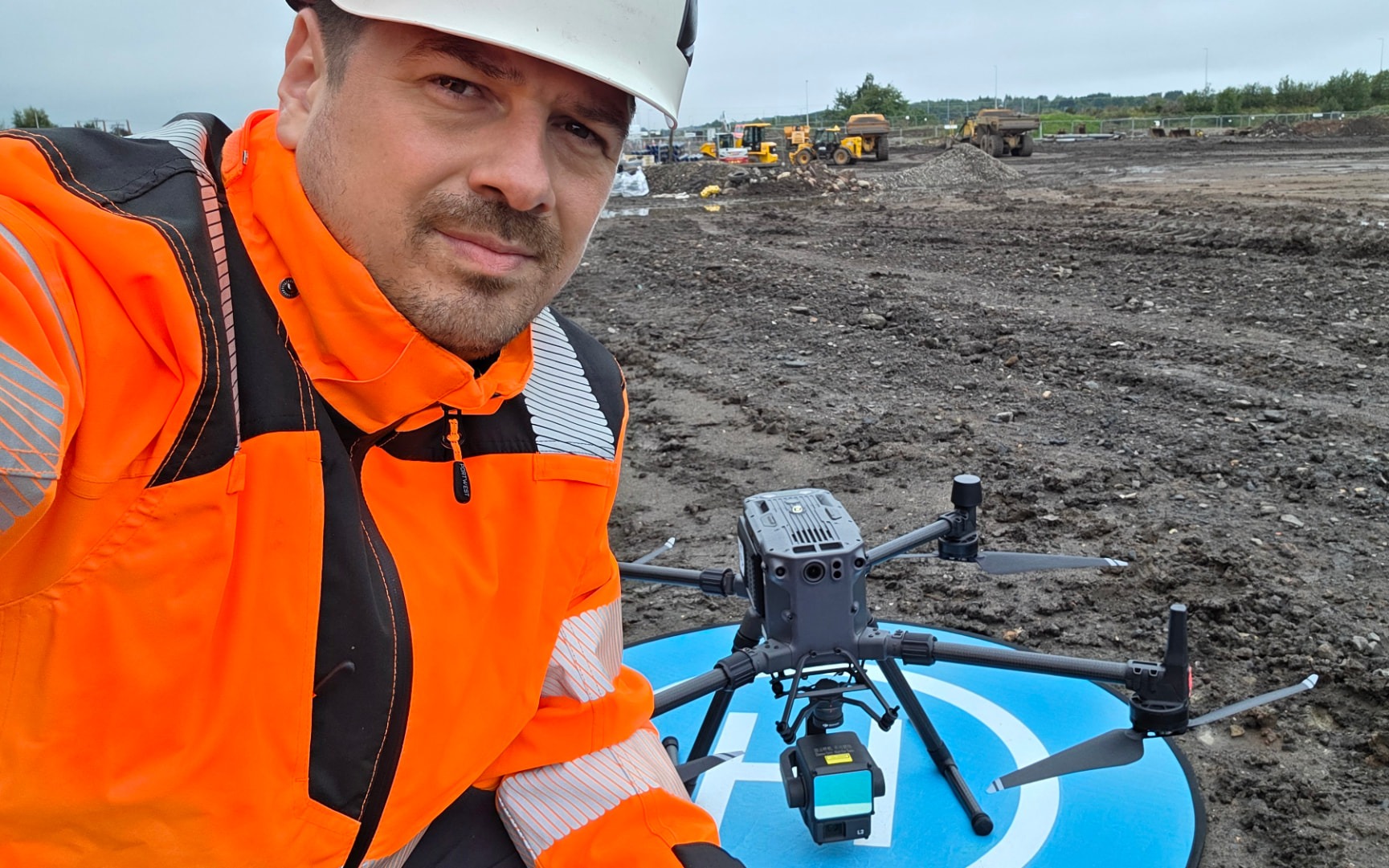 Stefan Niculescu on site in a hard hat and high-visibility jacket, beside a survey drone on its landing pad