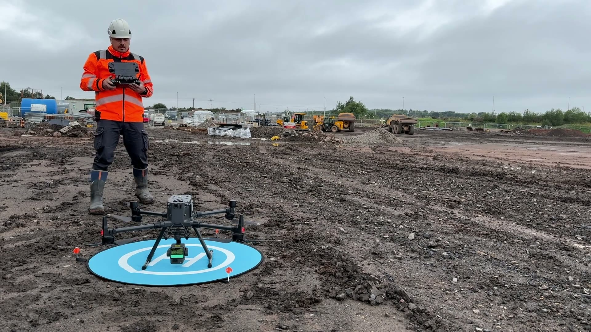 Stefan in hard hat and hi-vis flying a survey drone on a construction site.