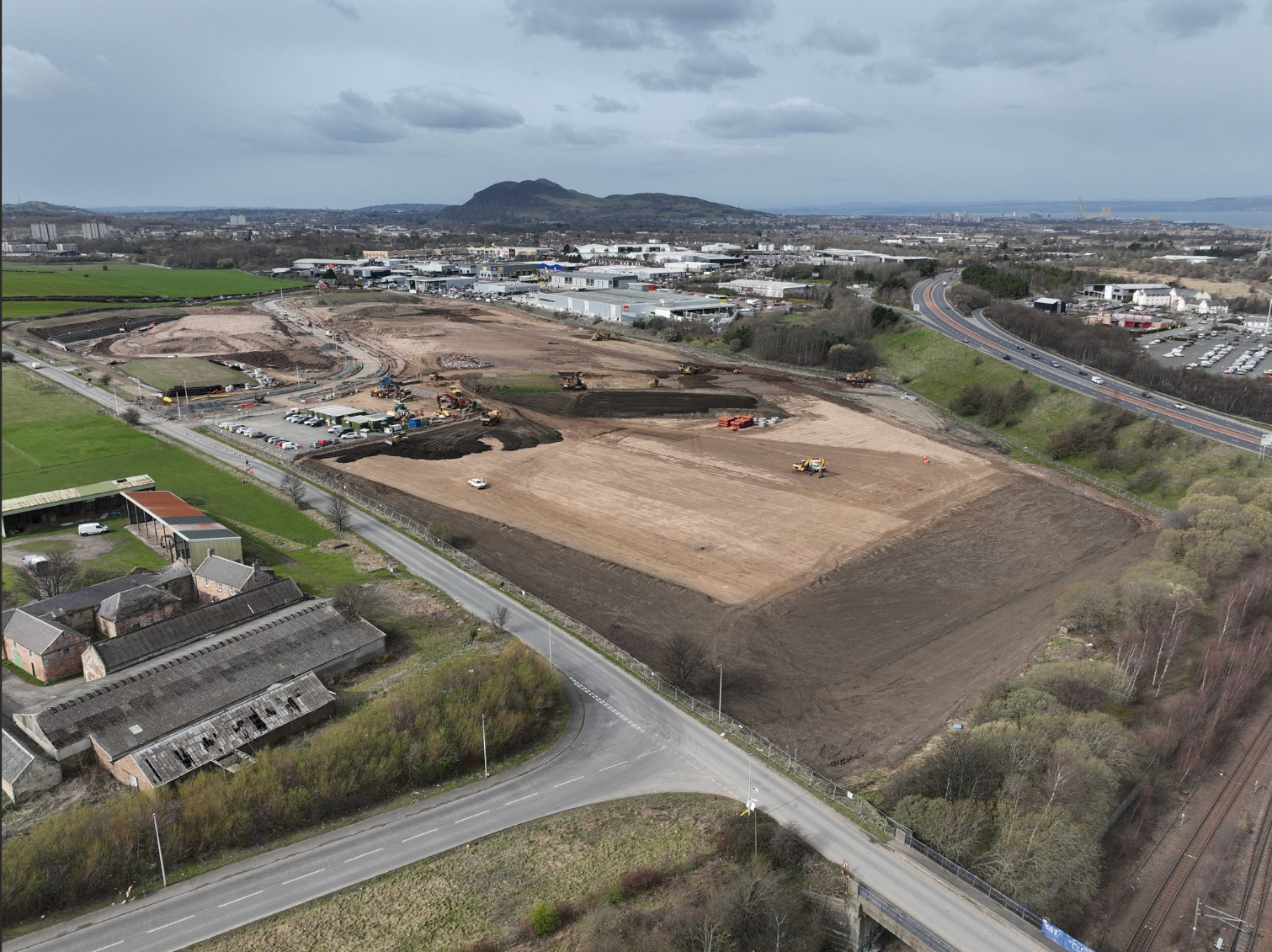 Aerial drone photo of the Shawfair Whitehills site during earthworks, with graded platforms, plant and stockpiles beside a main road and railway.